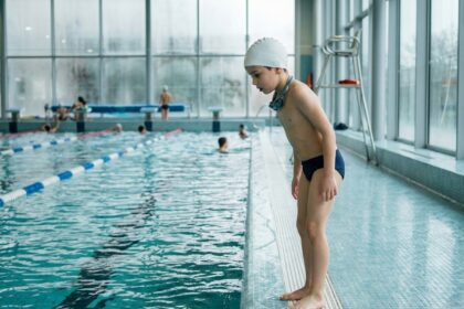 Enfant en maillot de bain au bord d'une piscine municipale à Paris, prêt pour son cours de natation extra-scolaire