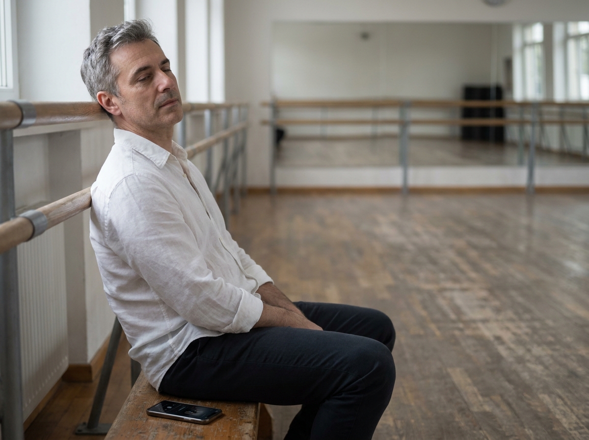 Homme d'une quarantaine d'années assis en bord de studio de danse, détendu, absorbé par la musique, illustrant le lâcher-prise