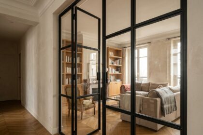 Porte verrière battante en acier noir et verre transparent installée dans un couloir d'appartement parisien, séparant le salon du couloir avec un effet de transparence partielle